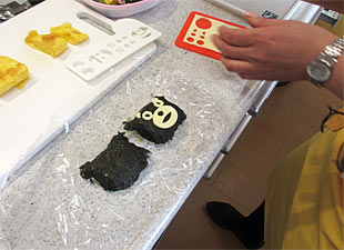 ご飯をかたどったものに、のりでくるみチーズで顔を作っていきます。さあ、なんのキャラクターかな?